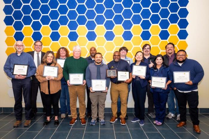 A large group of people stand posing with award plaques